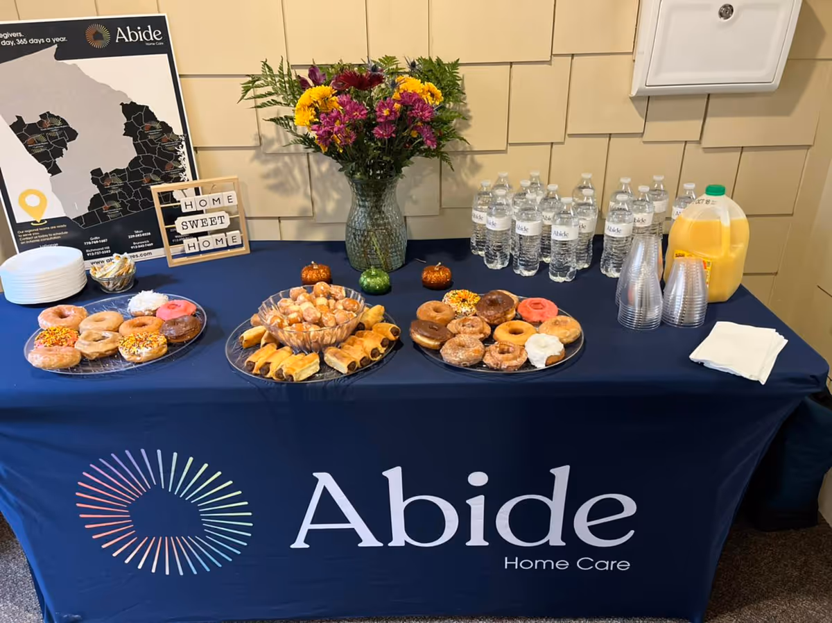 Table of donuts, pastries, water, juice, flowers, and Abide Home Care branding.