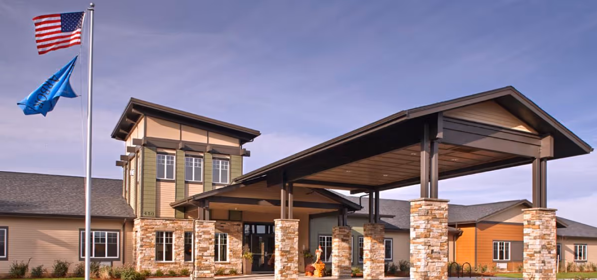 Exterior view of a senior living facility entrance with stone columns and flags.