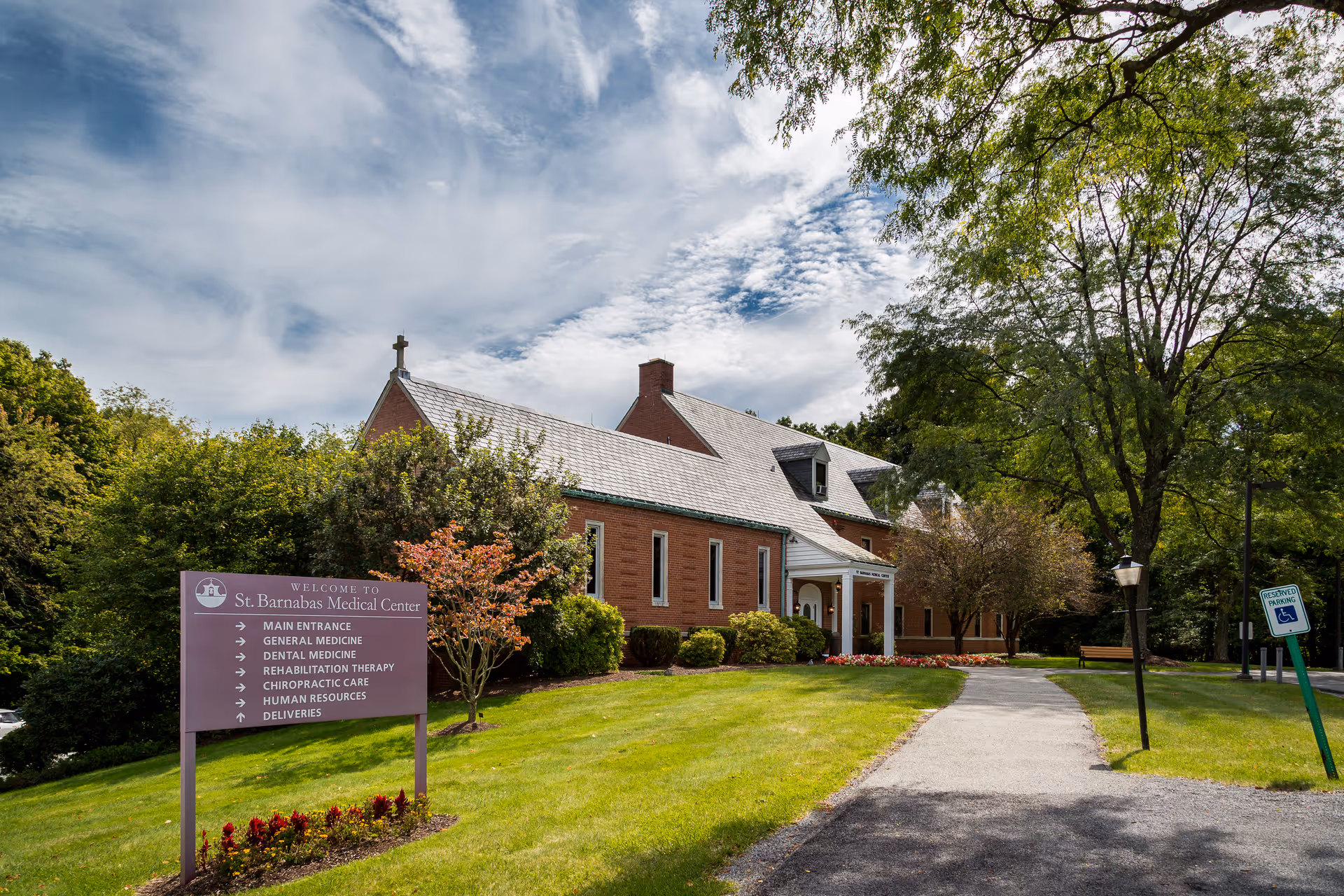 Brick building with a sign and entrance walkway, surrounded by trees and a manicured lawn.