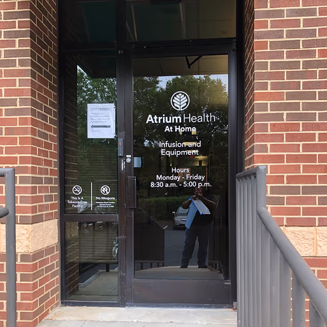 Glass door entrance with Atrium Health At Home signage on a brick building.