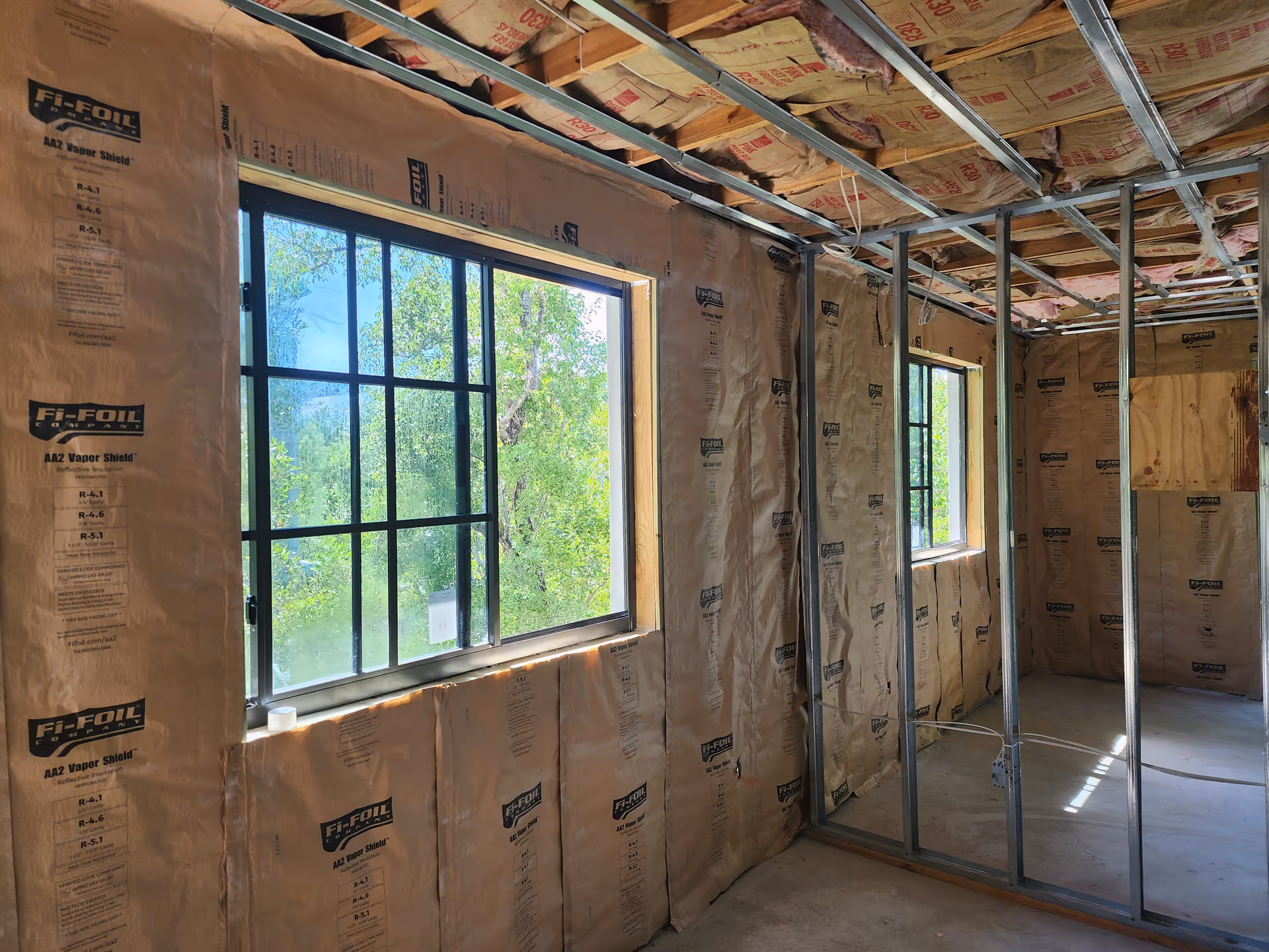 Unfinished interior room under renovation with exposed insulation, metal studs, and large windows.