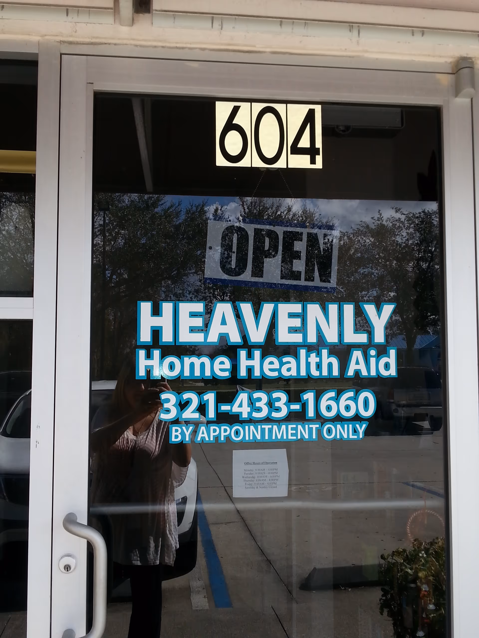 Glass storefront door displays 604, Heavenly Home Health Aid signage and OPEN, with tree reflections.
