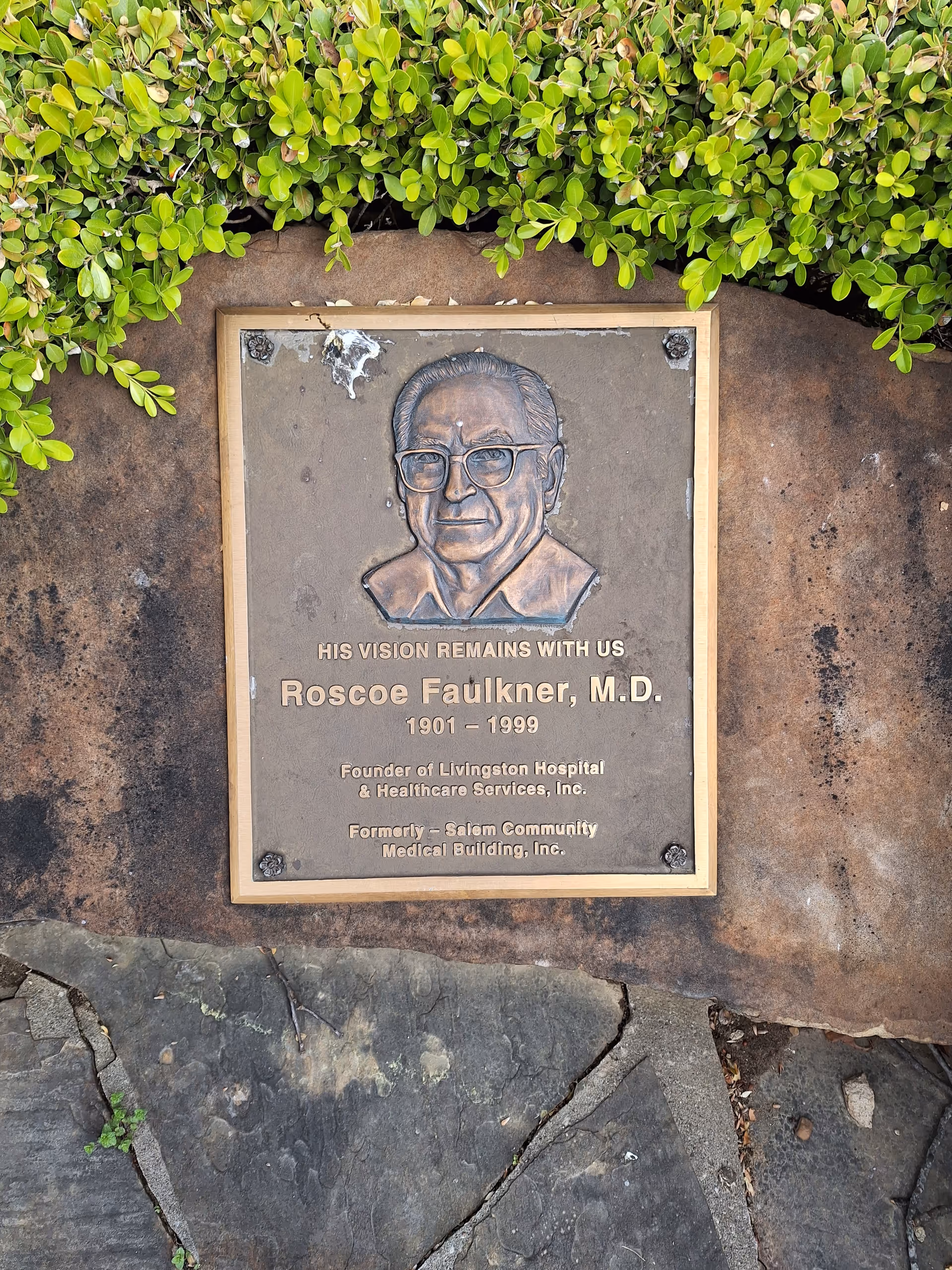Bronze plaque honoring Roscoe Faulkner, M.D., mounted on a stone wall with greenery.