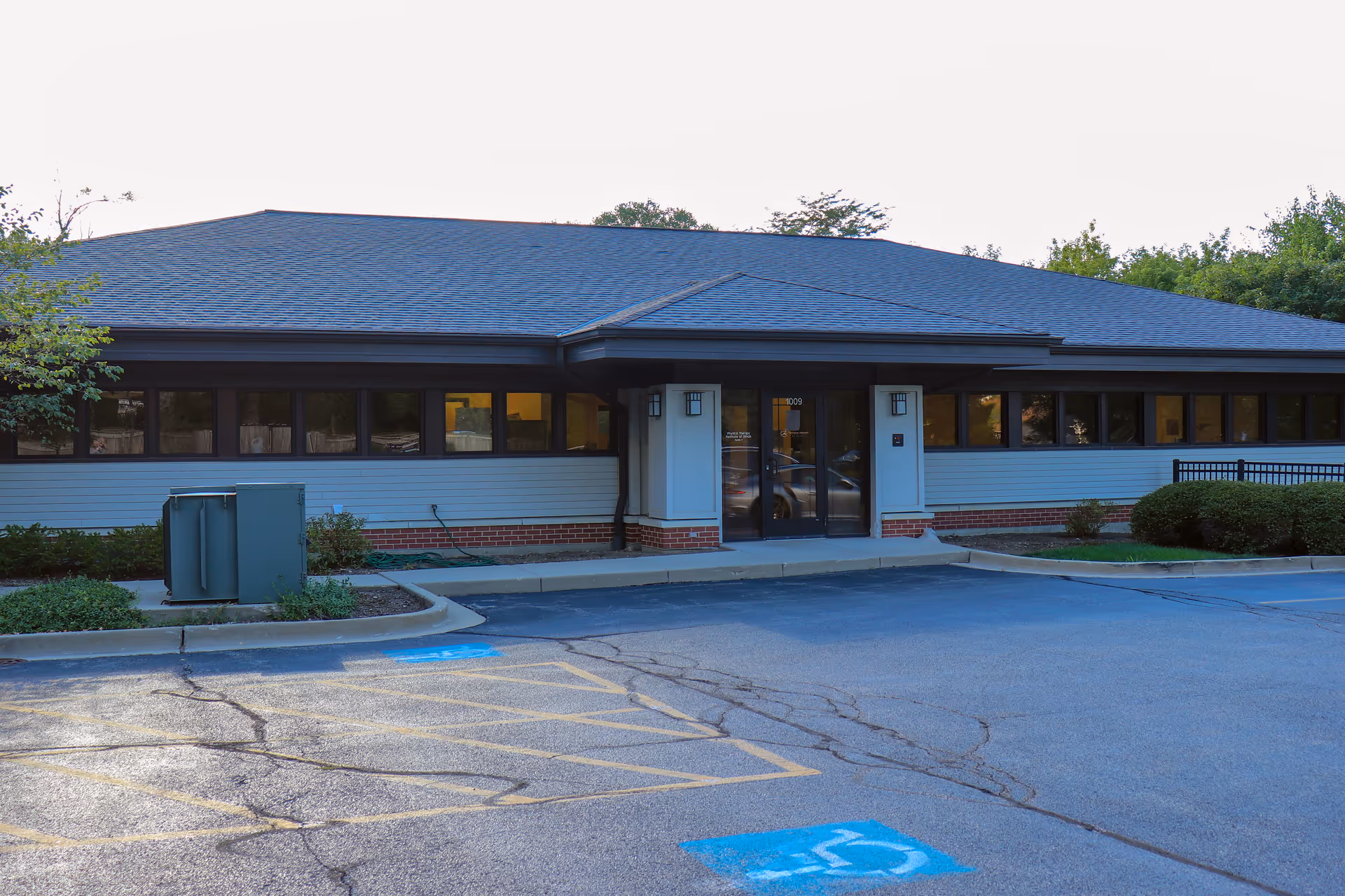 Single-story blue-siding building with glass entrance and handicap parking in front