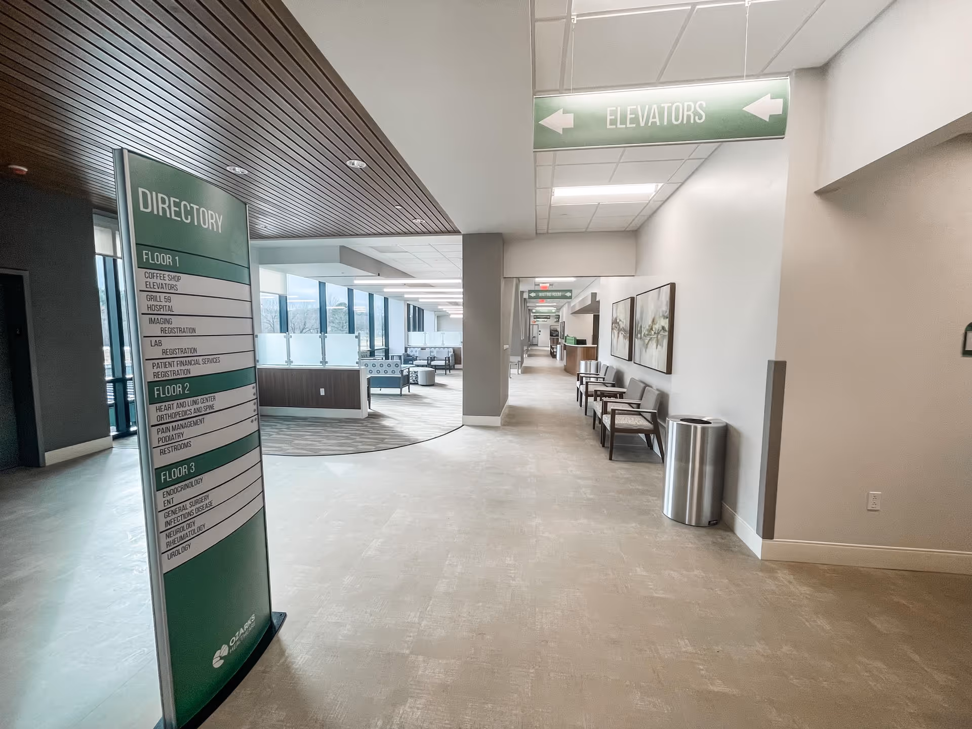 Interior hallway with directory sign, elevators, and seating along the wall.