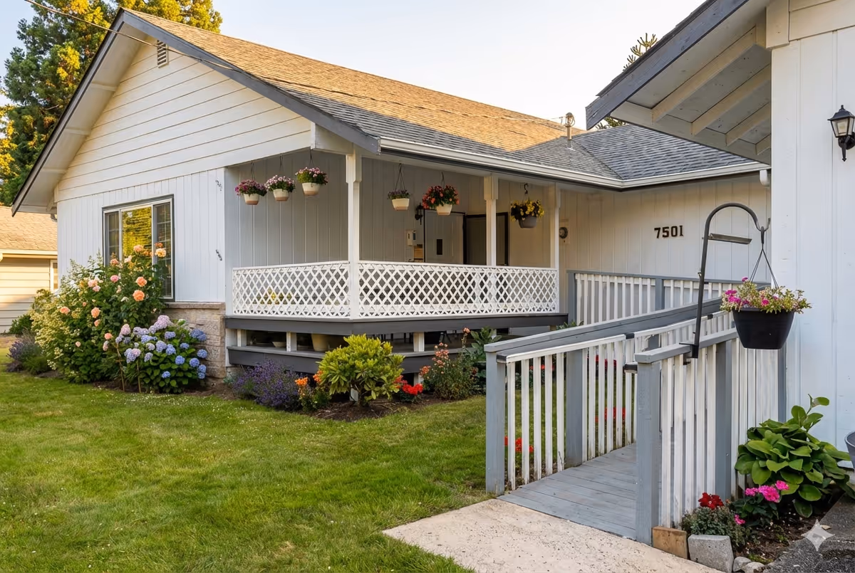 White single-story senior living home with front porch, hanging plants, and a ramp.
