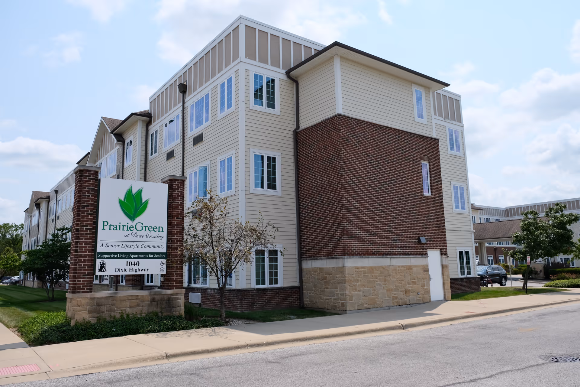 Exterior view of the Prairie Green at Dixie Crossing senior living building with a large entrance sign in front.