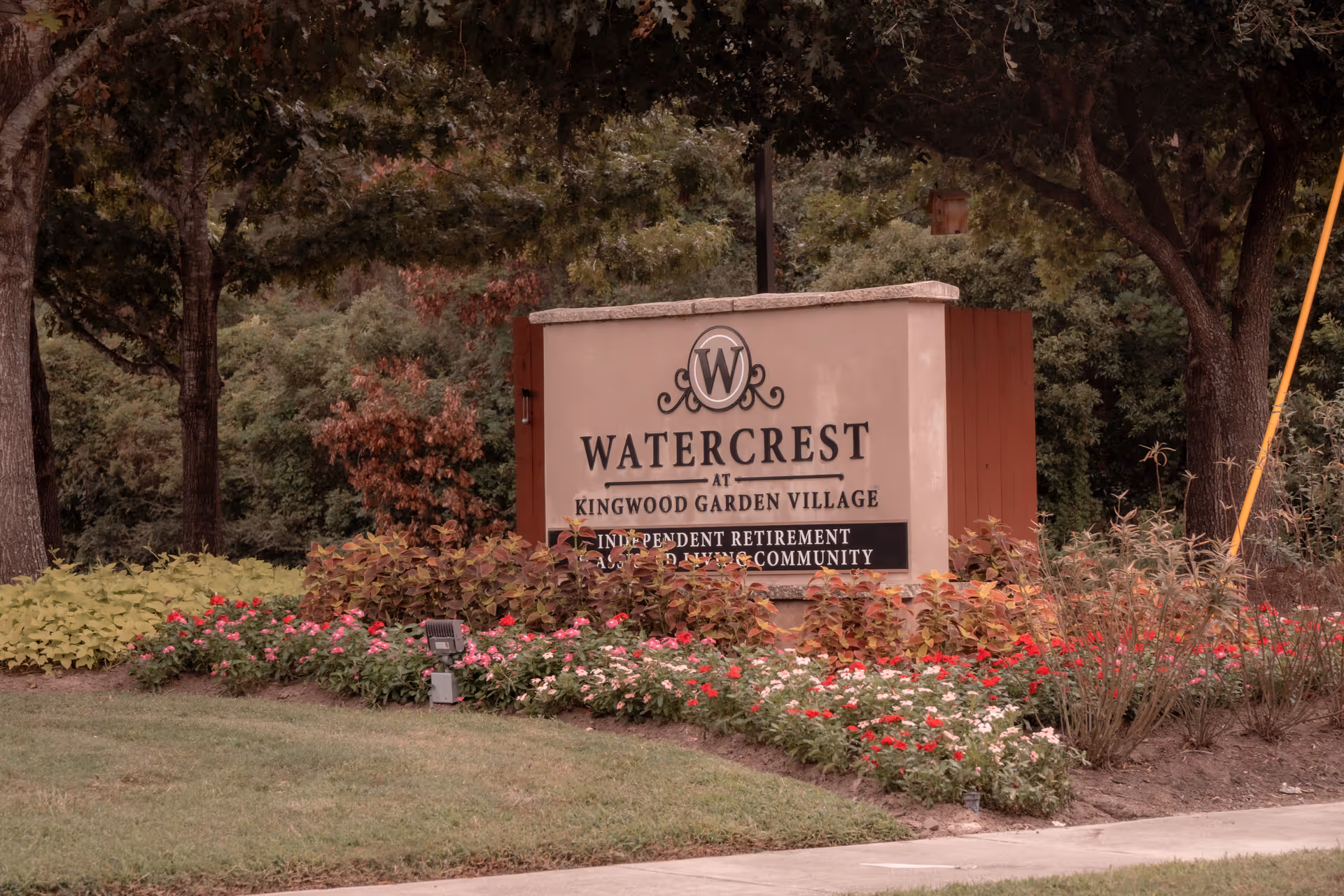Entrance sign reading "Watercrest at Kingwood Garden Village" surrounded by landscaped flowers and trees.