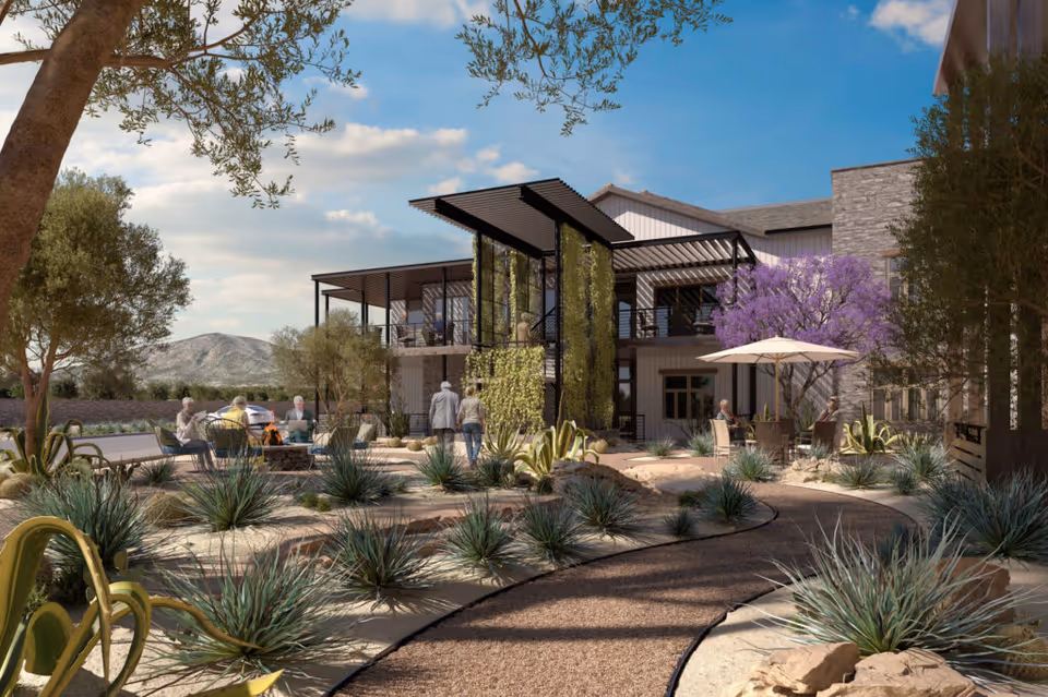Two-story senior living building with a landscaped courtyard, winding paths, seating areas and residents under a bright sky.