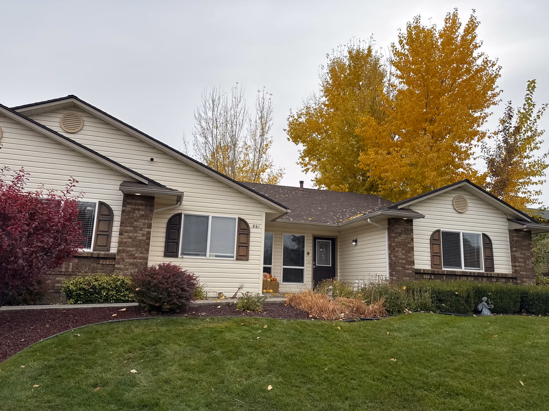 Single-story memory care building with beige siding, brick trim, and autumn-colored trees in foreground.
