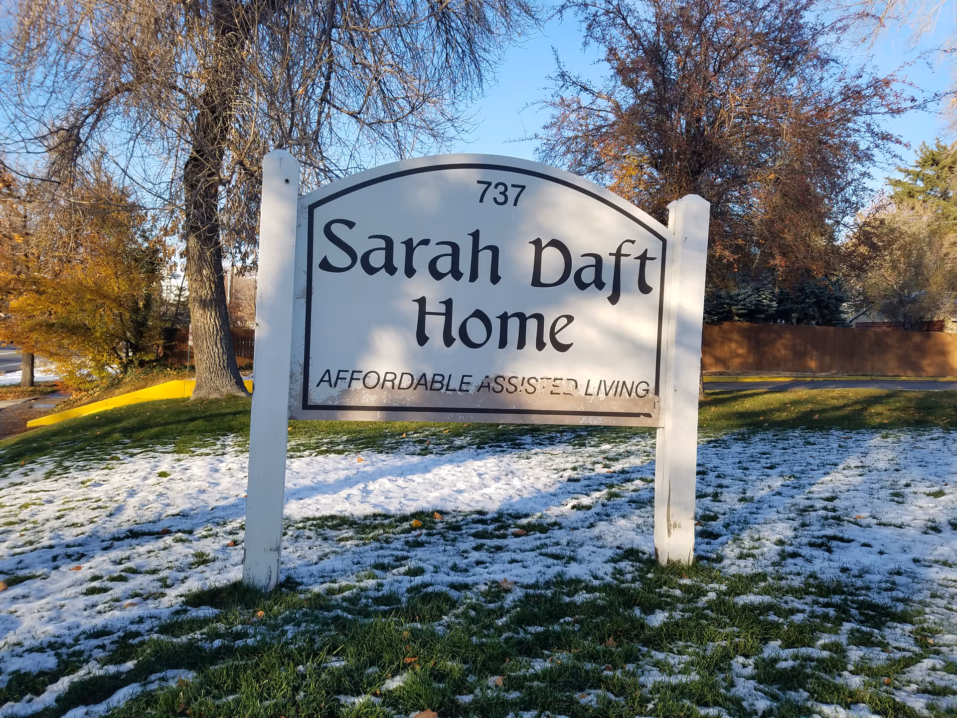 A large white sign reading Sarah Daft Home stands on posts in a snowy front yard.