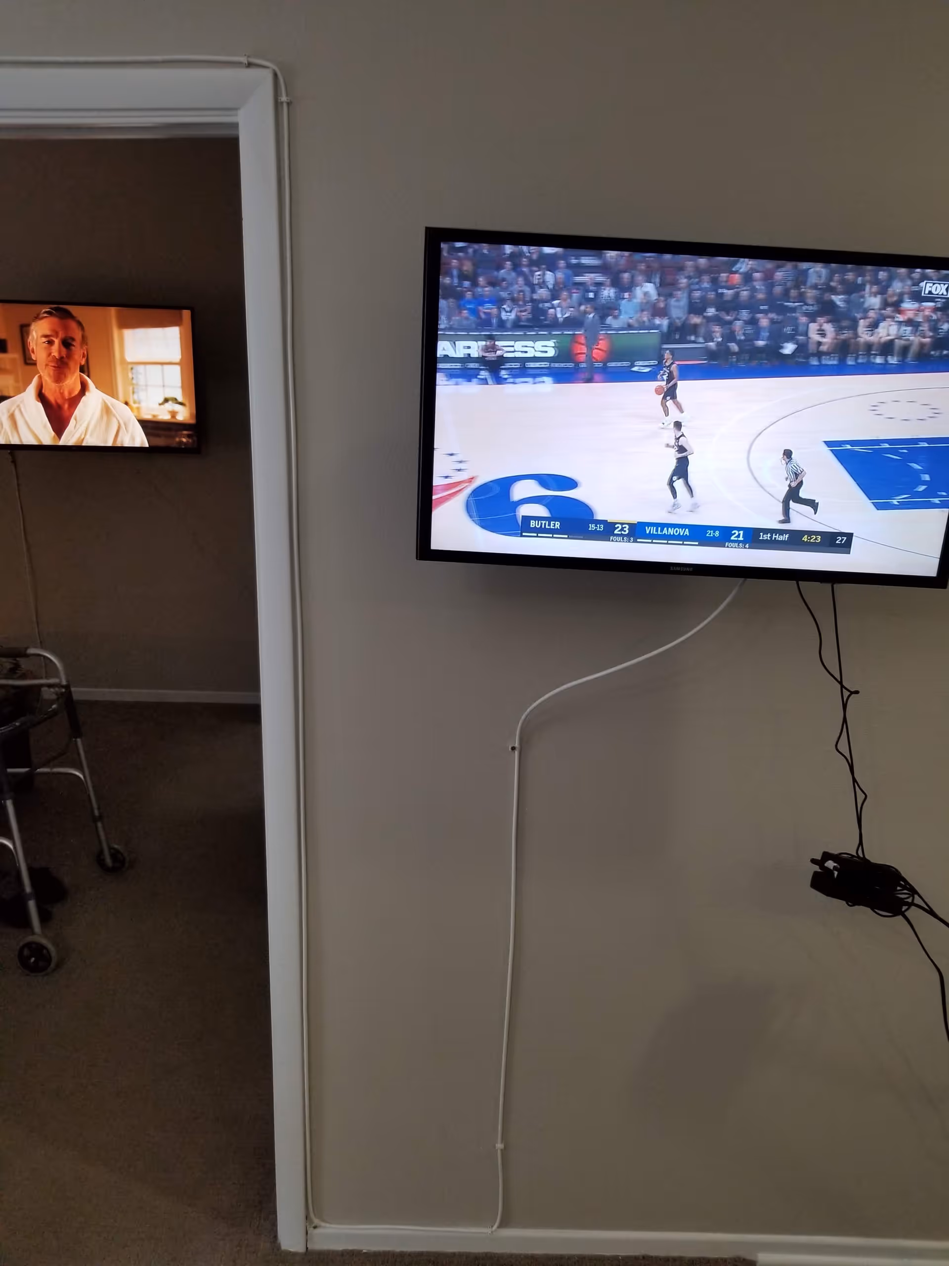 Interior of a senior living space with wall-mounted TV showing basketball game.