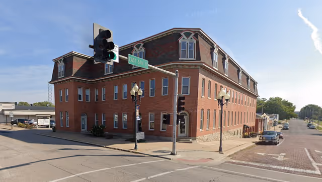 Brick, multi-story building on a street corner with traffic lights.