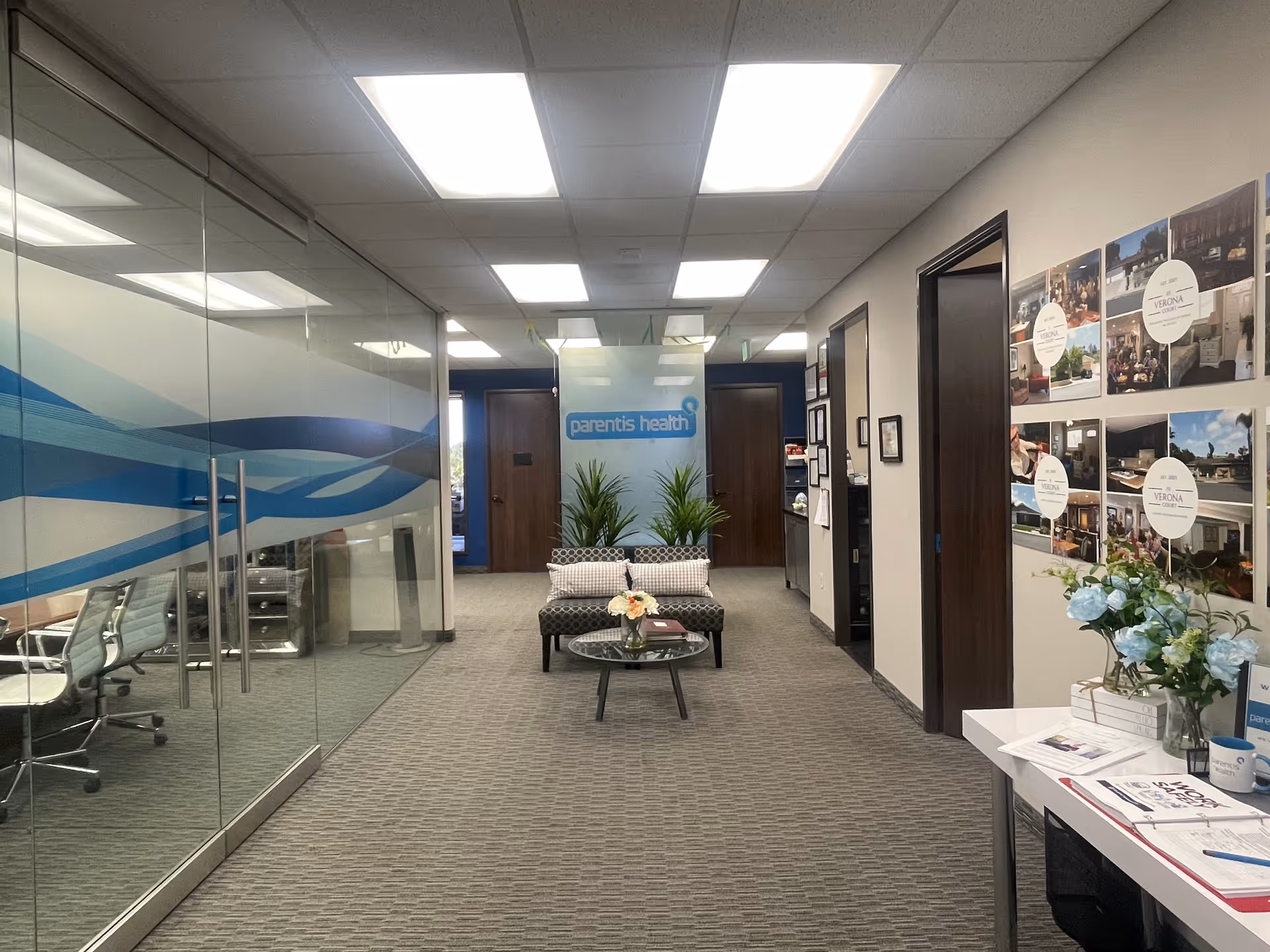 Interior lobby of a senior health facility with glass walls, seating area, and plants.