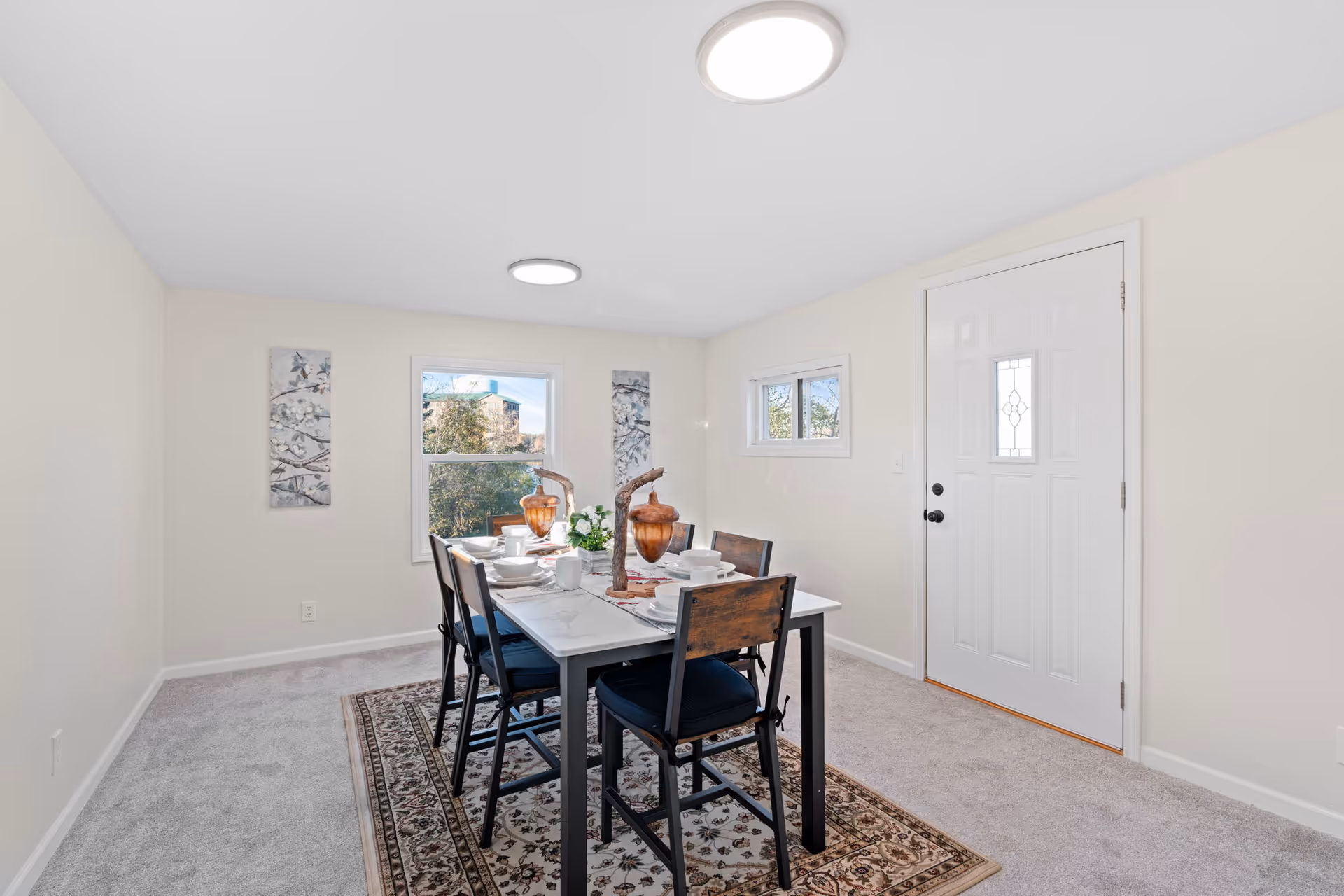 A dining room with a table set for dinner and a front entry door.