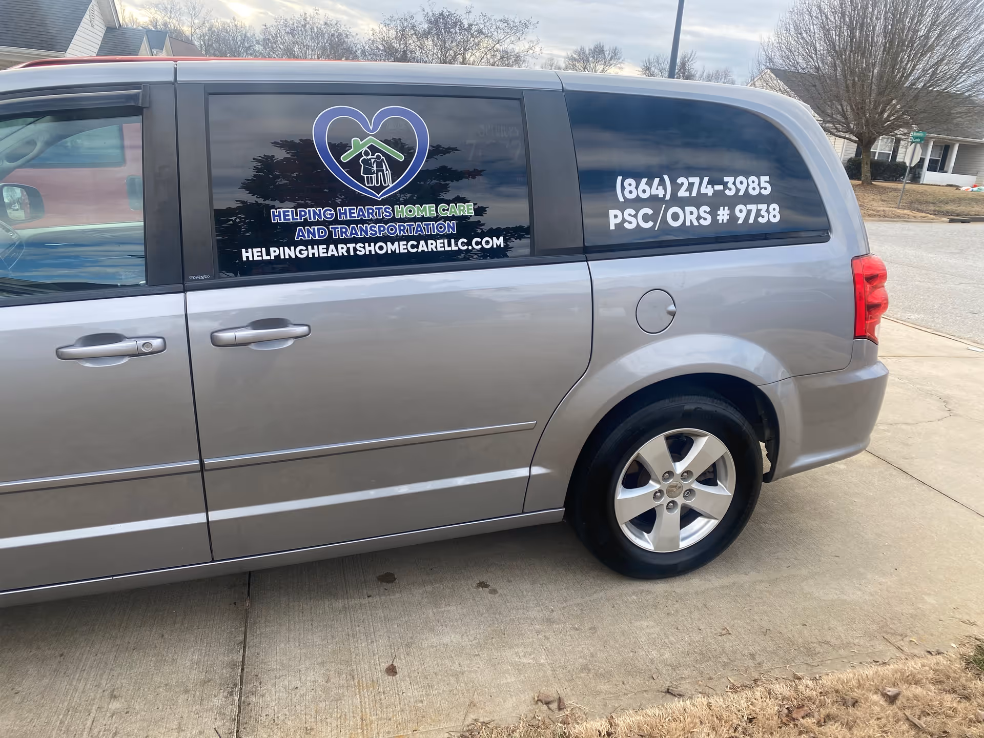 Silver van with Helping Hearts Home Care logo, contact info, parked on driveway.