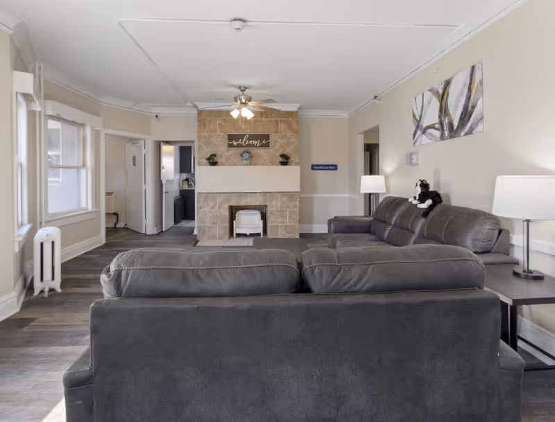 Cozy lounge area in a senior facility with sectional sofas, fireplace, and decorative artwork.