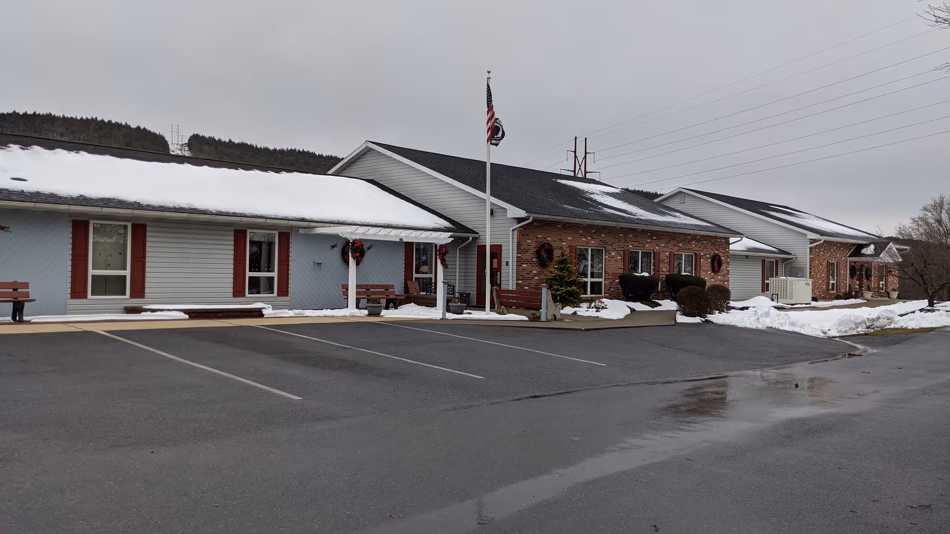 Exterior view of a single-story senior care facility with brick siding, snow, and benches.