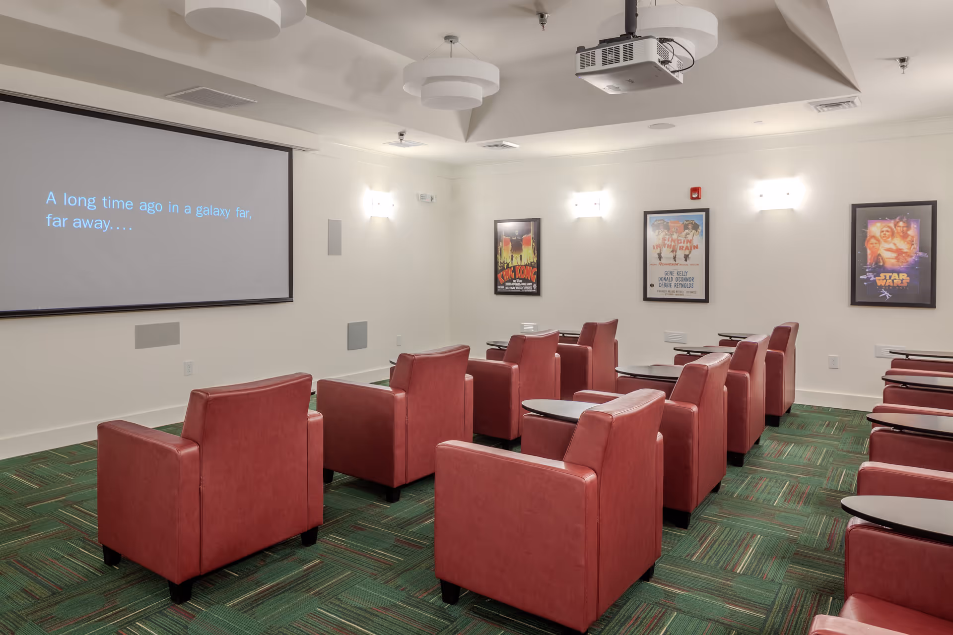 Projection screen shows text in a senior living facility media room with red theater chairs.