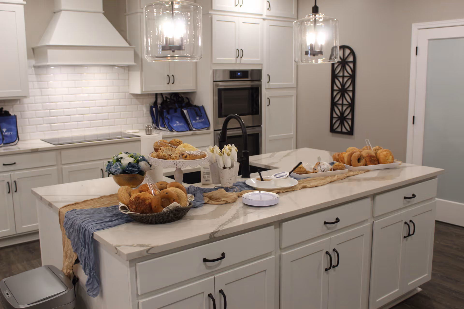 White kitchen with marble island, pendant lights, and pastries on display.