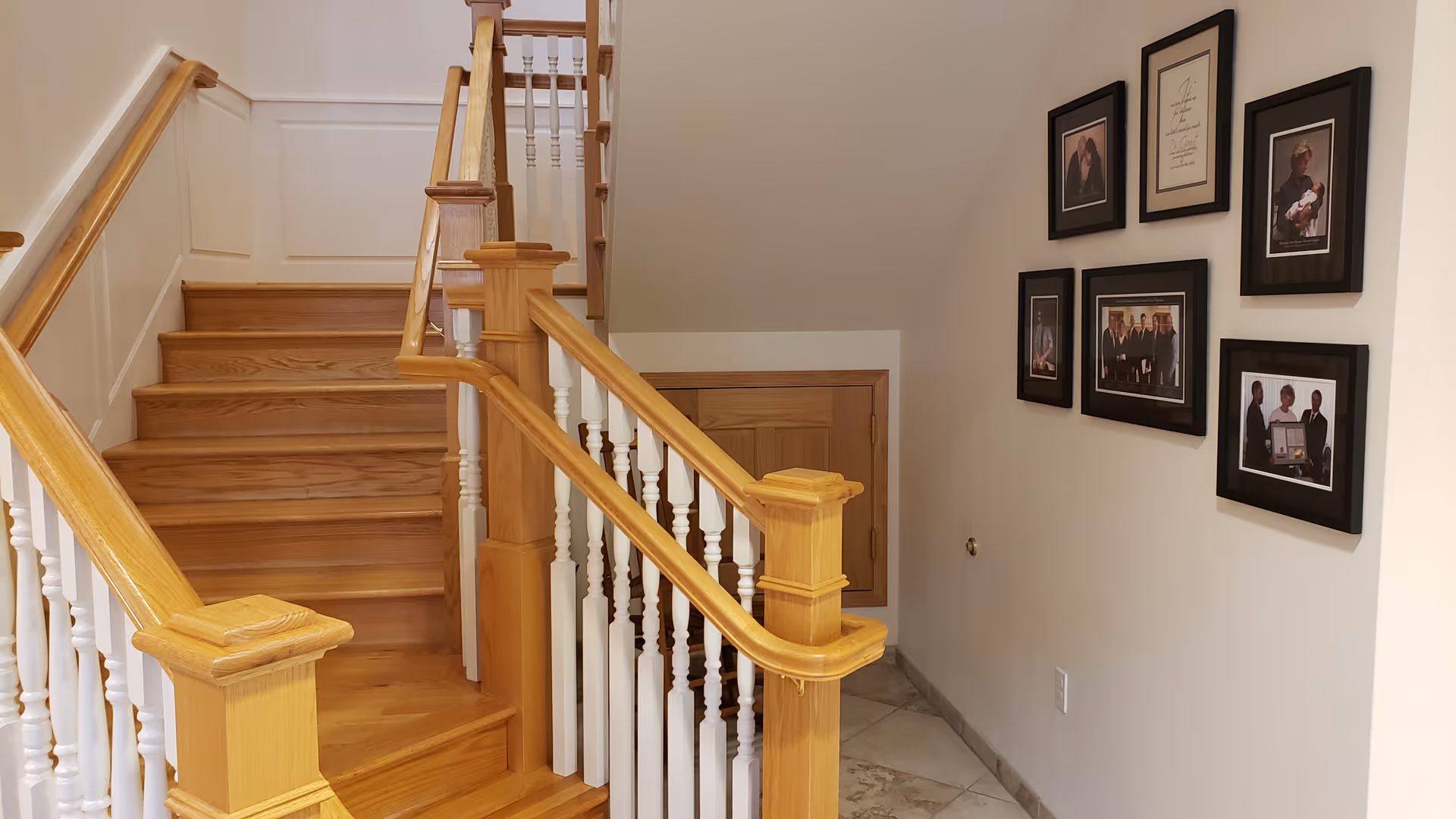 Wooden staircase with white spindles and framed photos along a beige hallway.