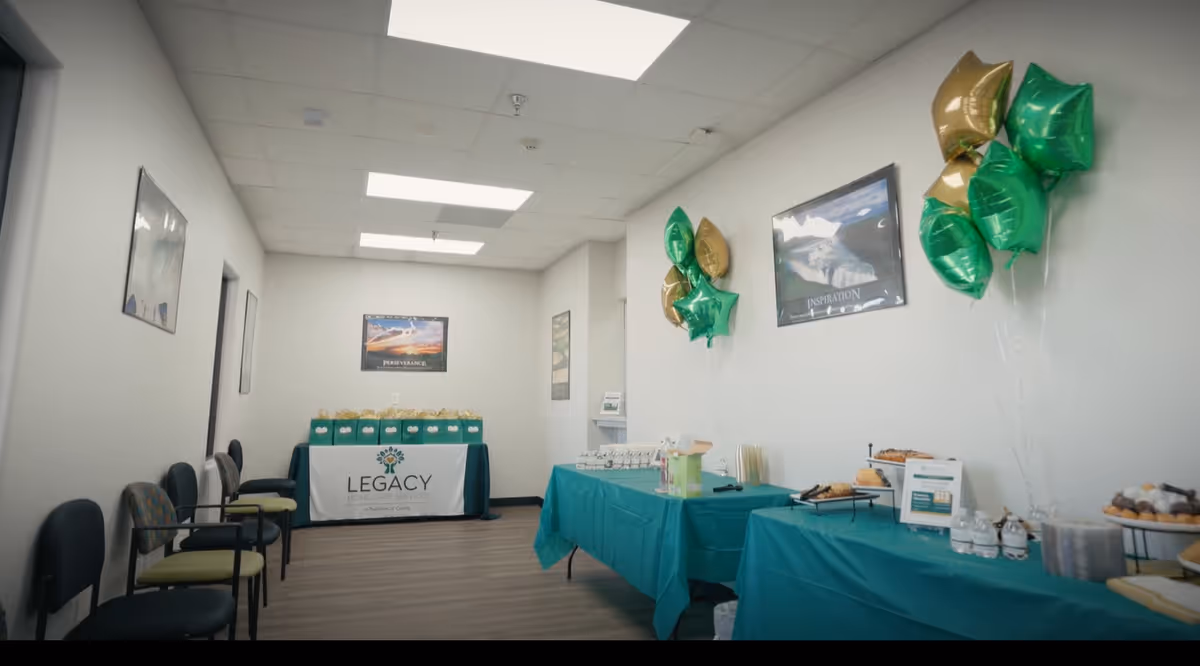 Event setup in a Legacy facility hall with teal tablecloths, balloons, and snacks.