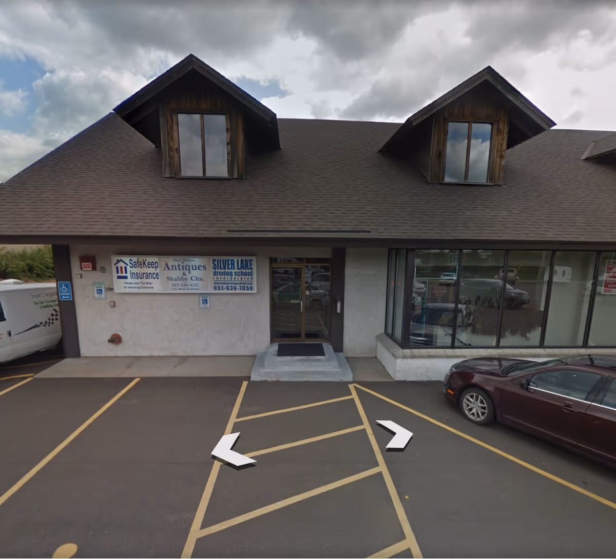 Front of a beige commercial building with windows, signboards, and a parking lot.