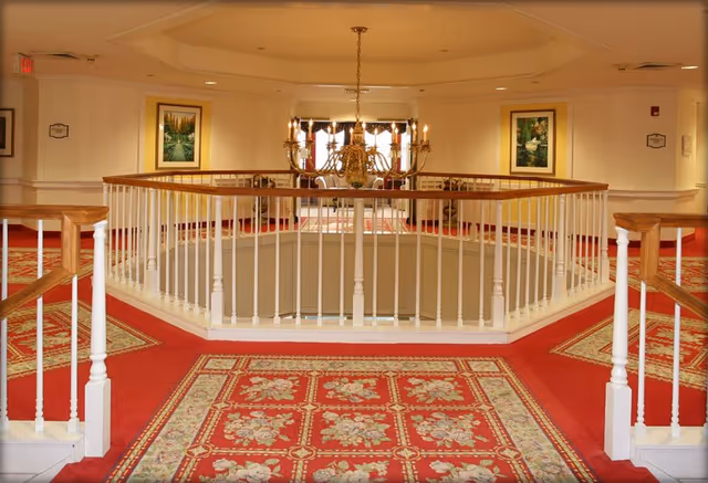 Wide view of an interior atrium with chandelier, railings, and red patterned carpet.
