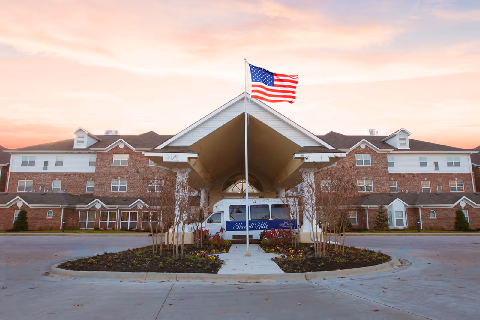 Exterior view of Sherrill Hills Retirement Resort with entrance, flag, and shuttle bus.