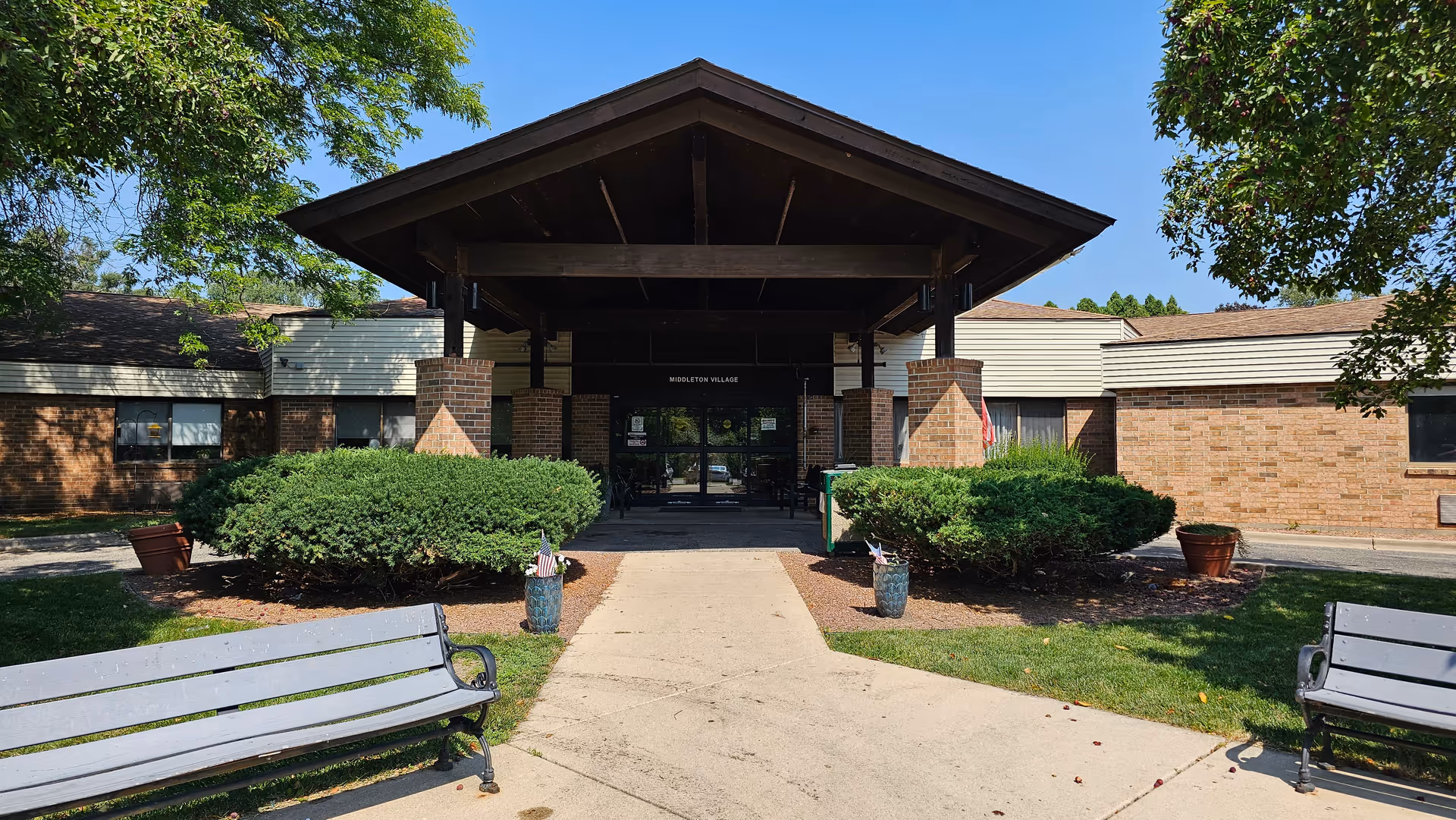 Wide view of Villa at Middleton Village entrance with brick facade, benches, and greenery.
