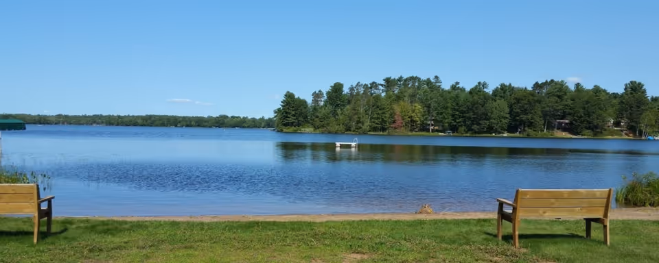 Two wooden benches face a tranquil lake with trees along the shoreline.