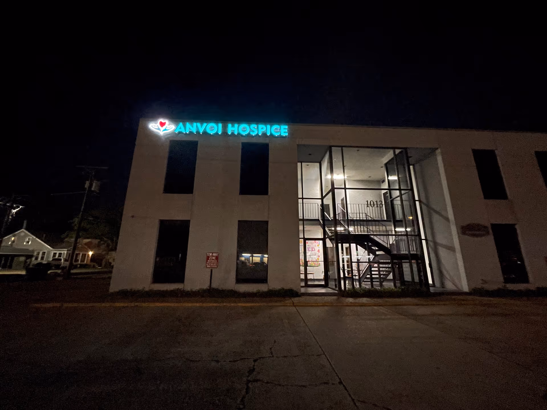 Nighttime exterior of Anvoi Hospice building with illuminated sign and glass entrance.