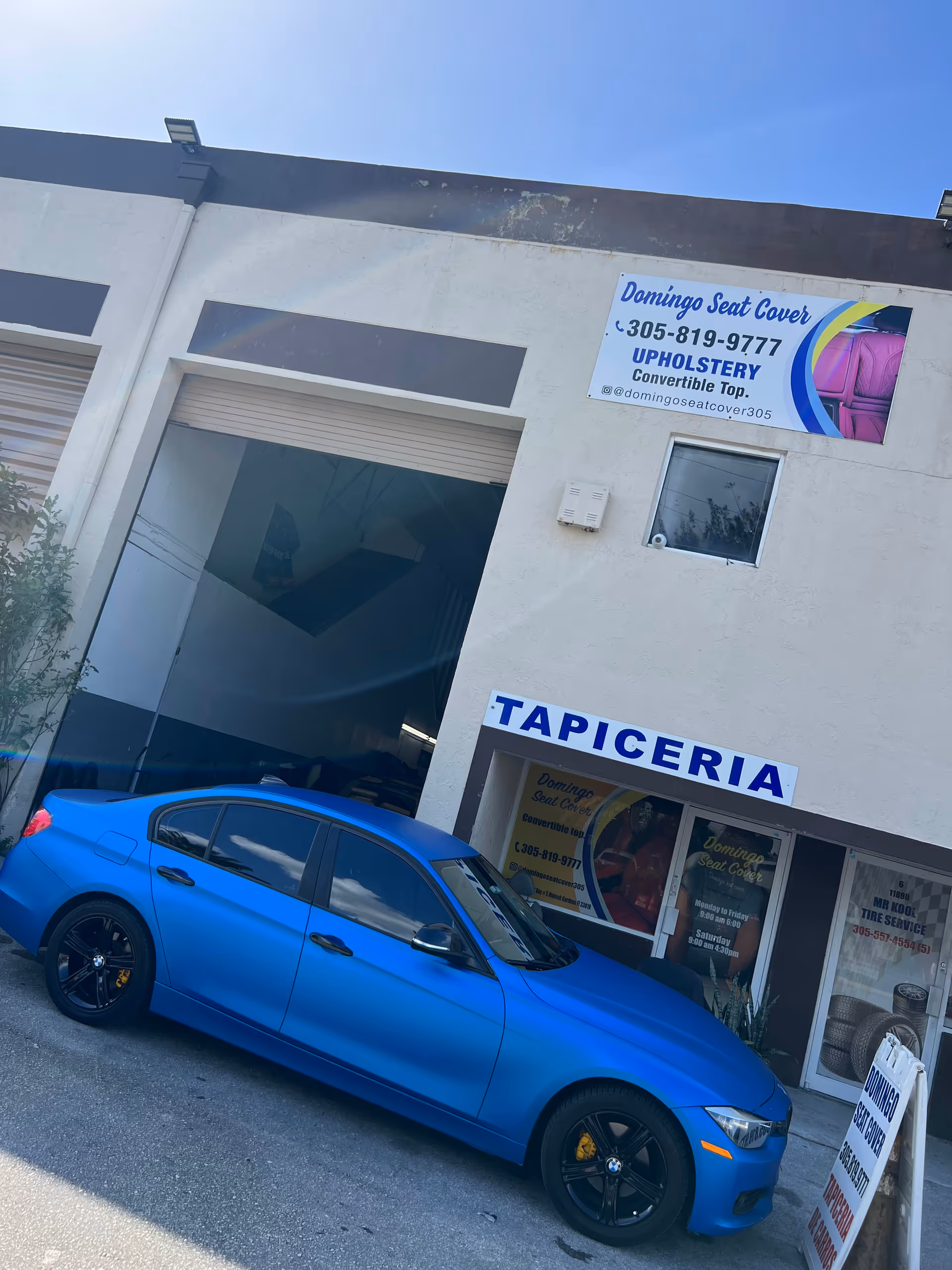 Blue sedan parked outside a storefront with Tapiceria signage.
