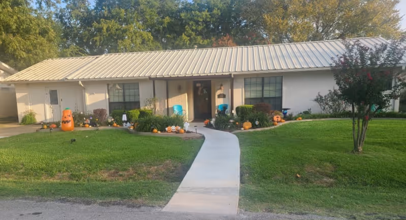 Single-story white facility facade with curved walkway, pumpkins, and autumn landscaping in front