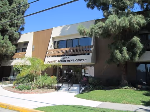 Front view of Downey Retirement Center entrance with steps, railing, and surrounding trees.