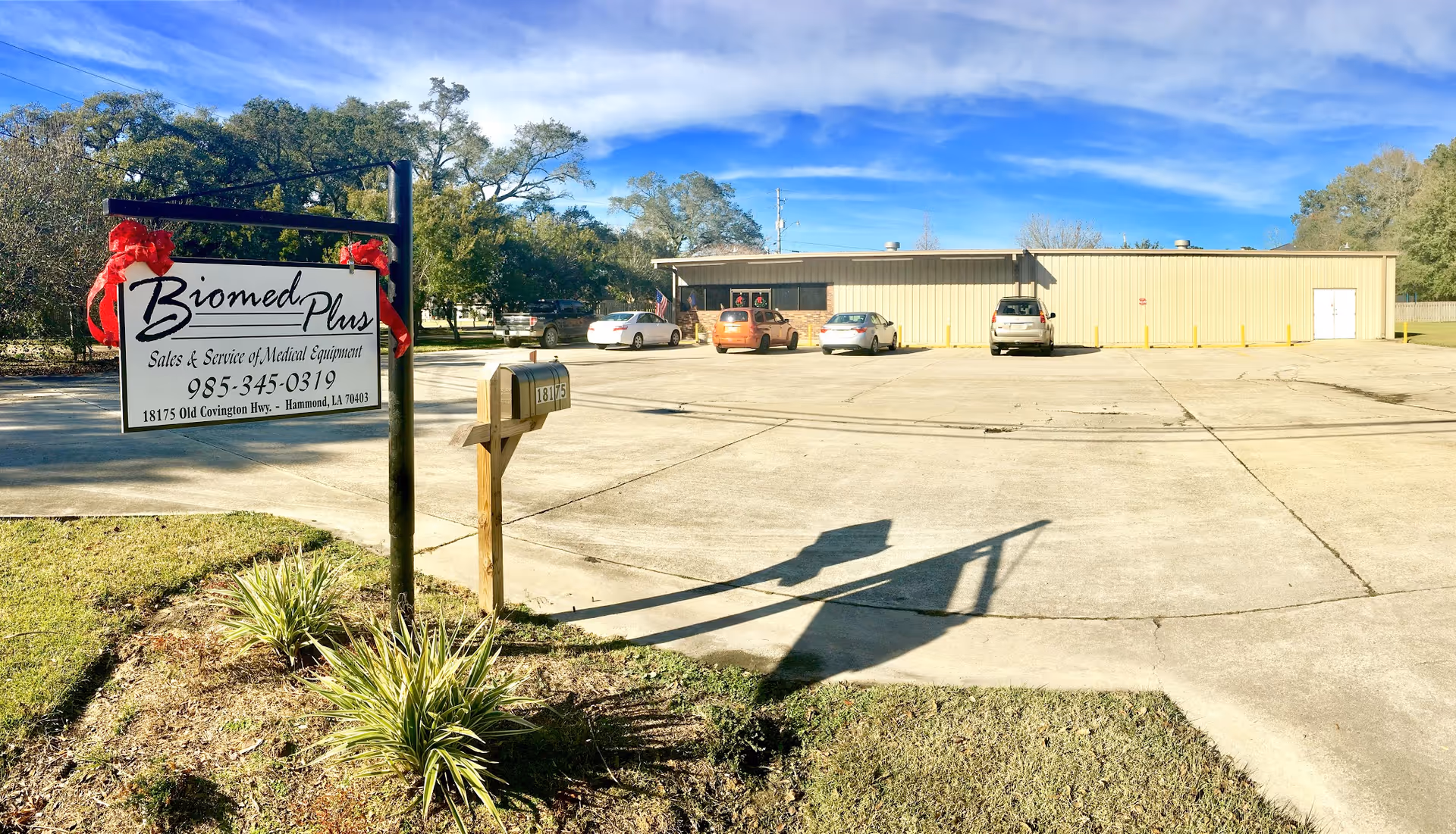 Exterior view of Biomed Plus facility with sign and parked cars.
