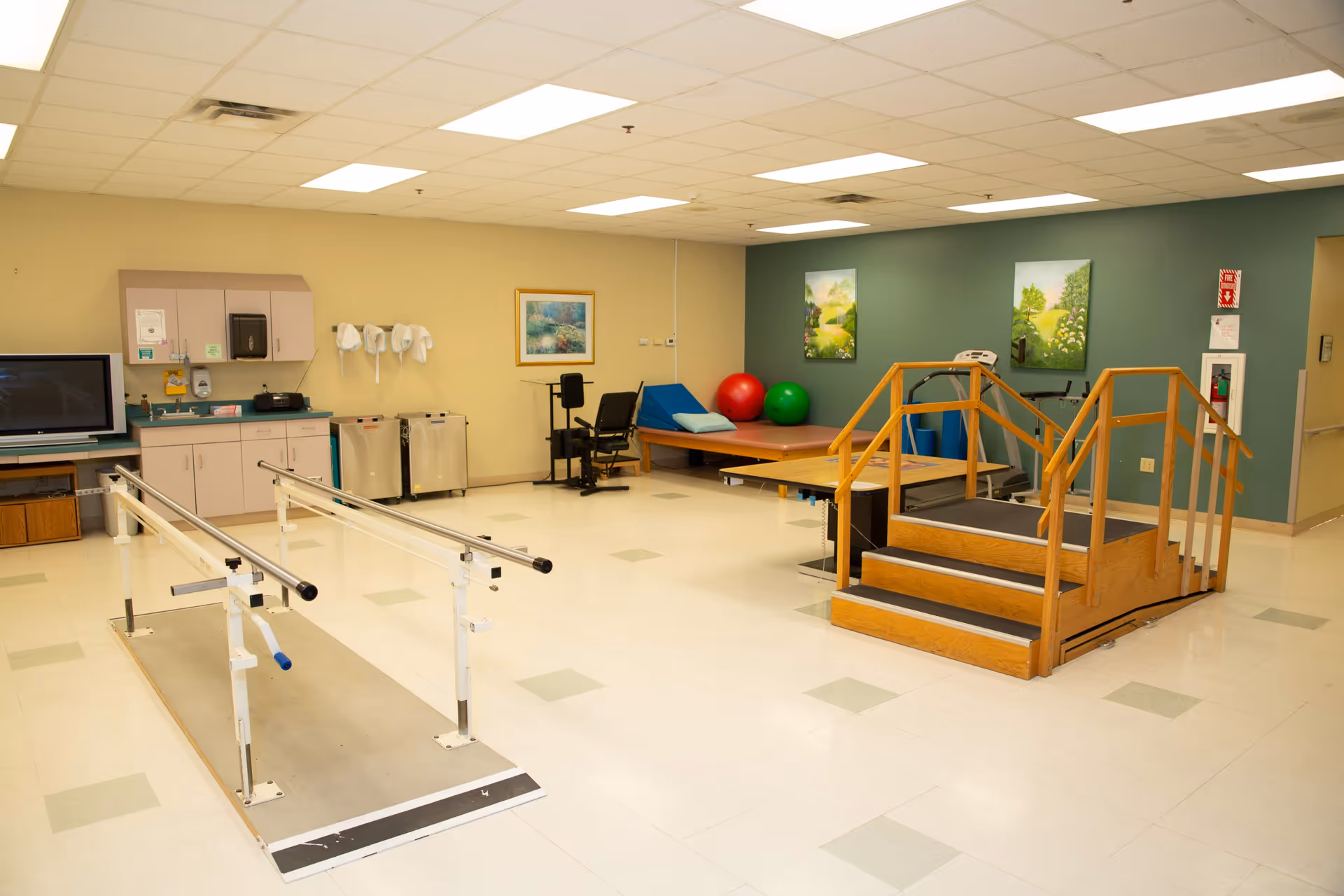 Interior rehab gym in a senior living facility with parallel bars and therapy equipment.