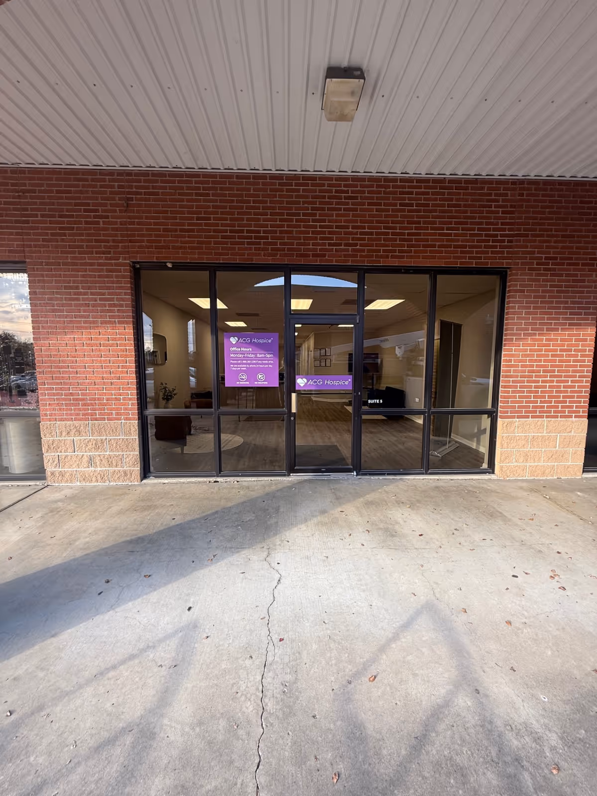 Brick building entrance with glass doors displaying ACG Hospice signage and a visible lobby inside.