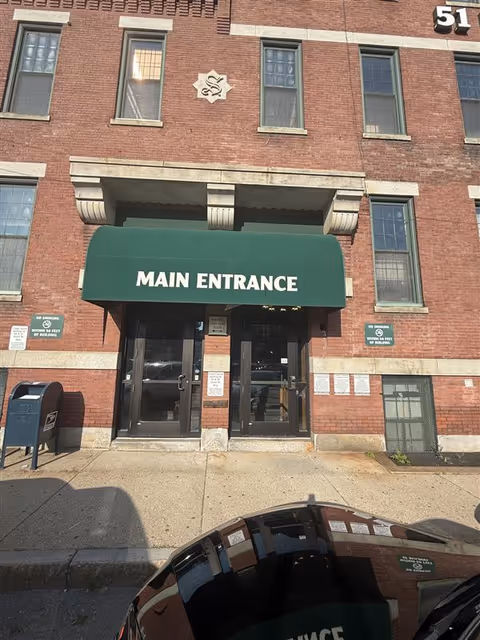 Brick building facade with a green Main Entrance awning over glass doors.