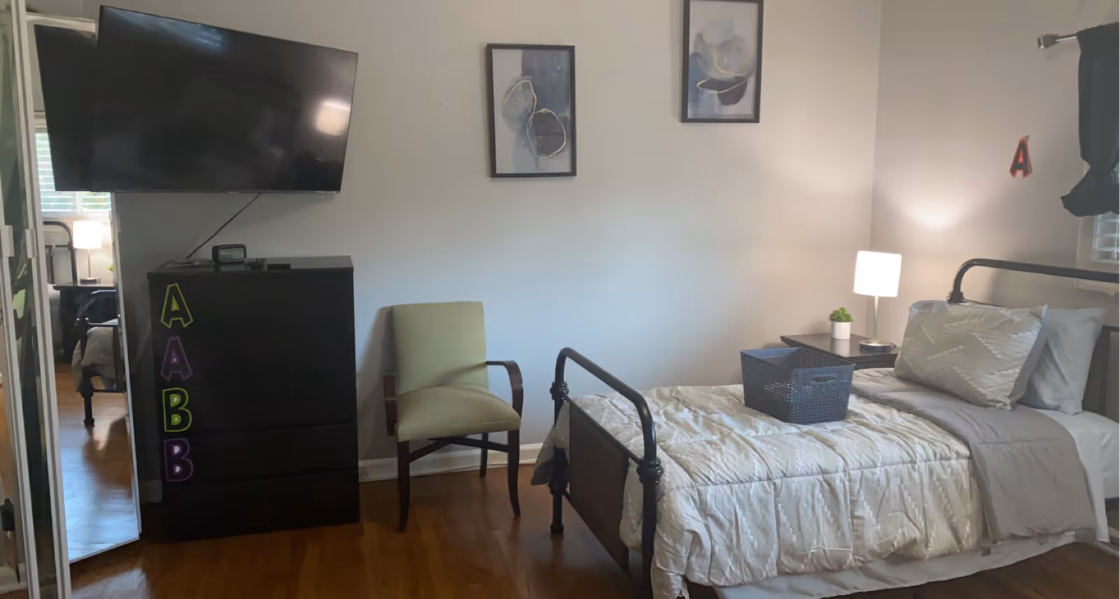 Cozy bedroom with a bed, dresser, mounted TV, chair, and a nightstand.