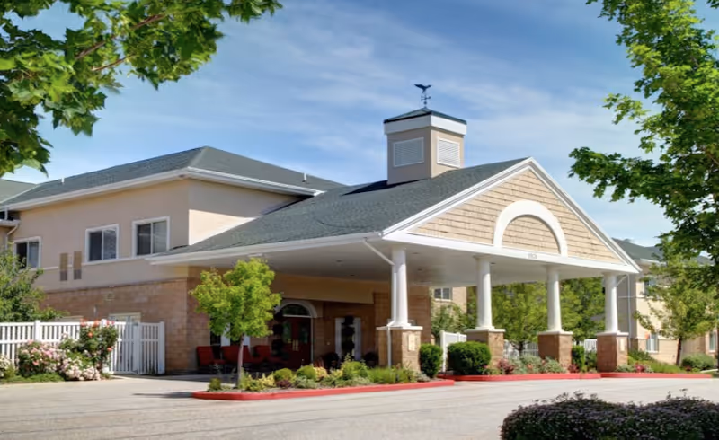 Covered main entrance and portico of a two-story senior living building with columns, landscaping, and a driveway.