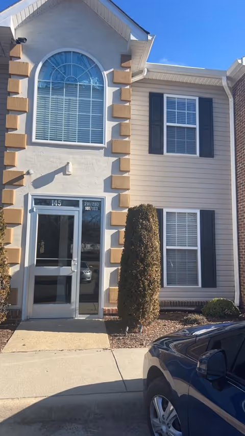 Exterior of a two-story facility with arched window, beige siding, stone corner accents, and shrubs.