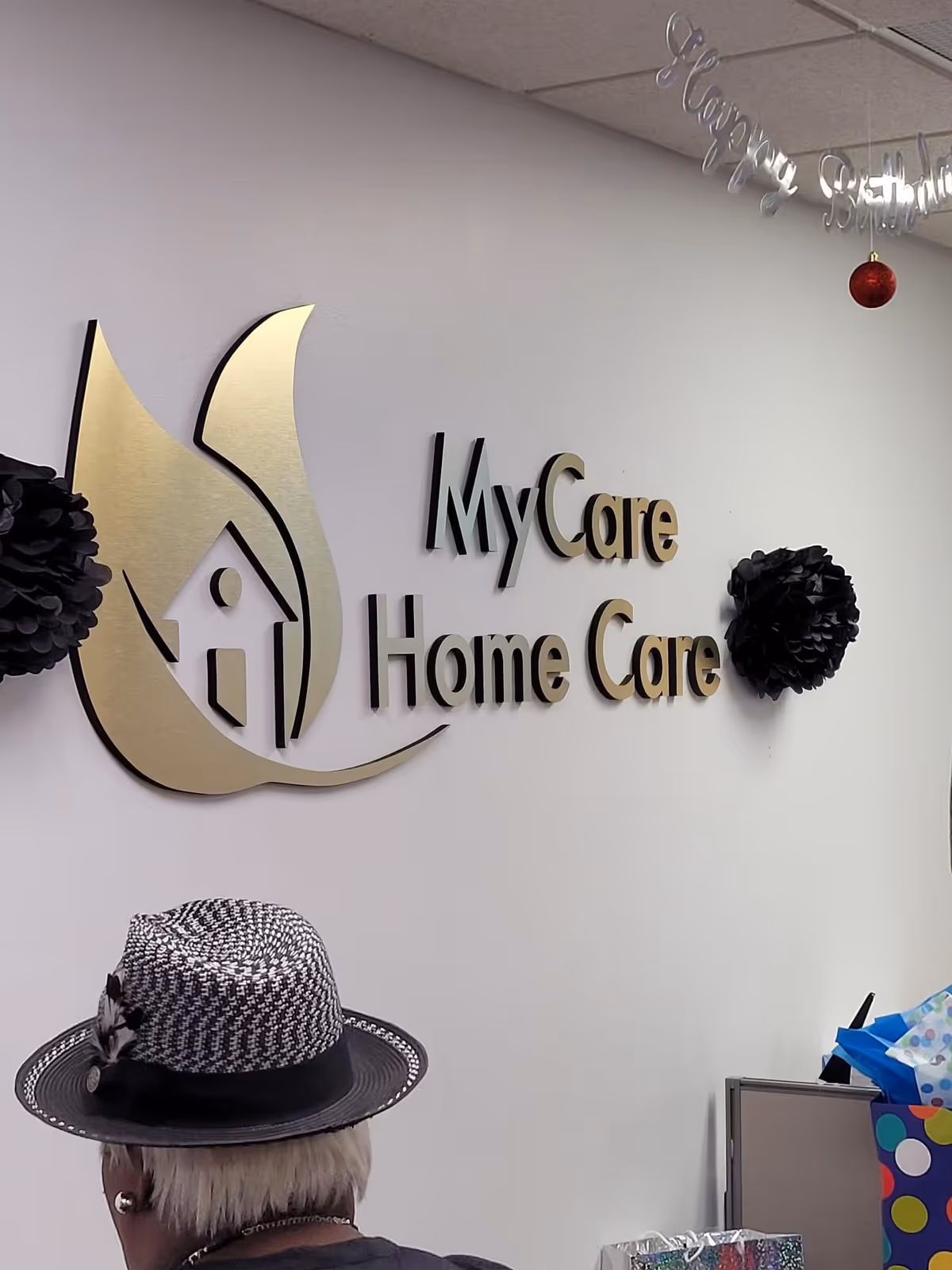Interior wall featuring the MyCare Home Care logo; a person wearing a hat stands nearby.
