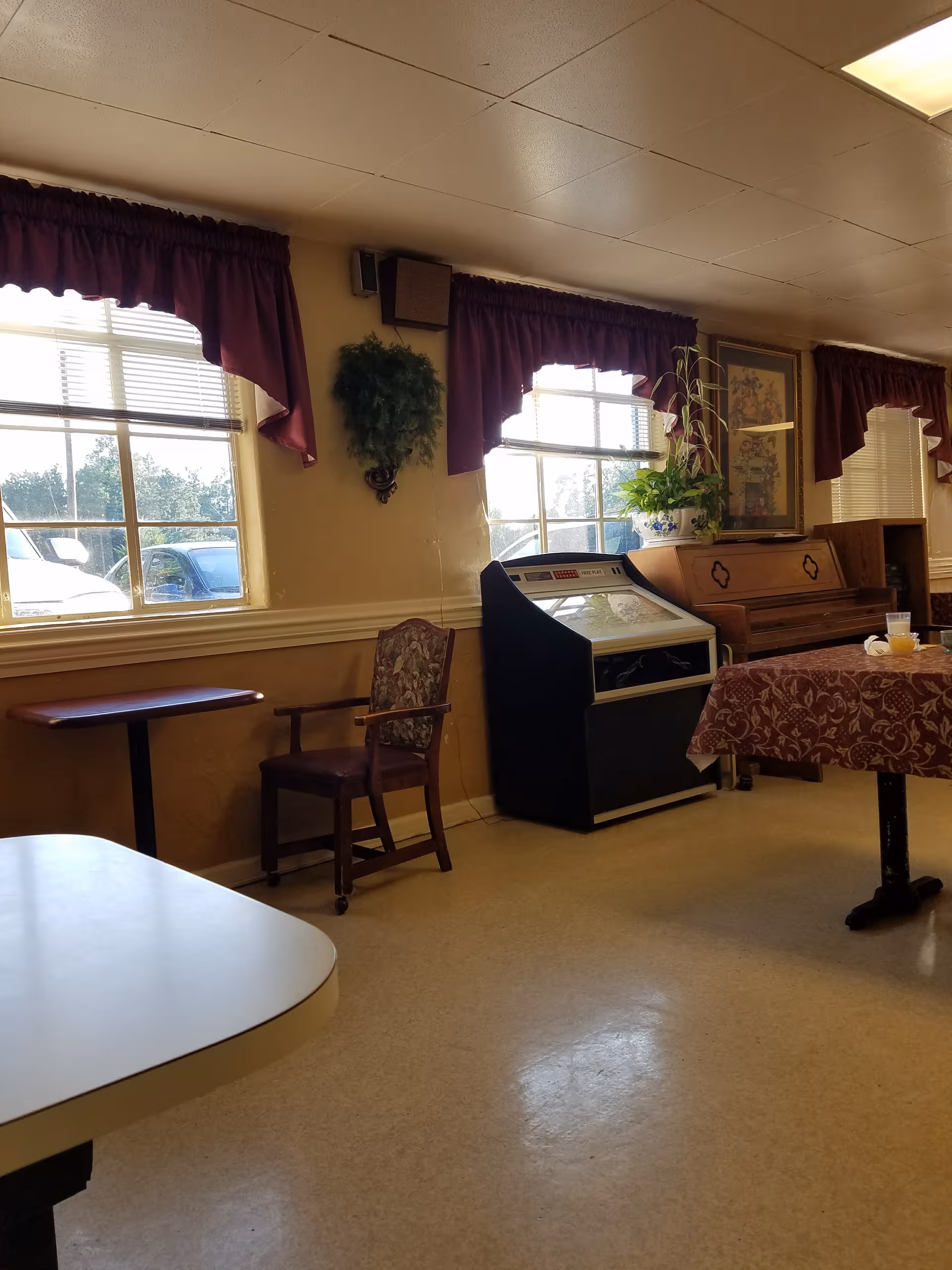 Dining room scene with tables, chairs, windows, curtains, and a piano.
