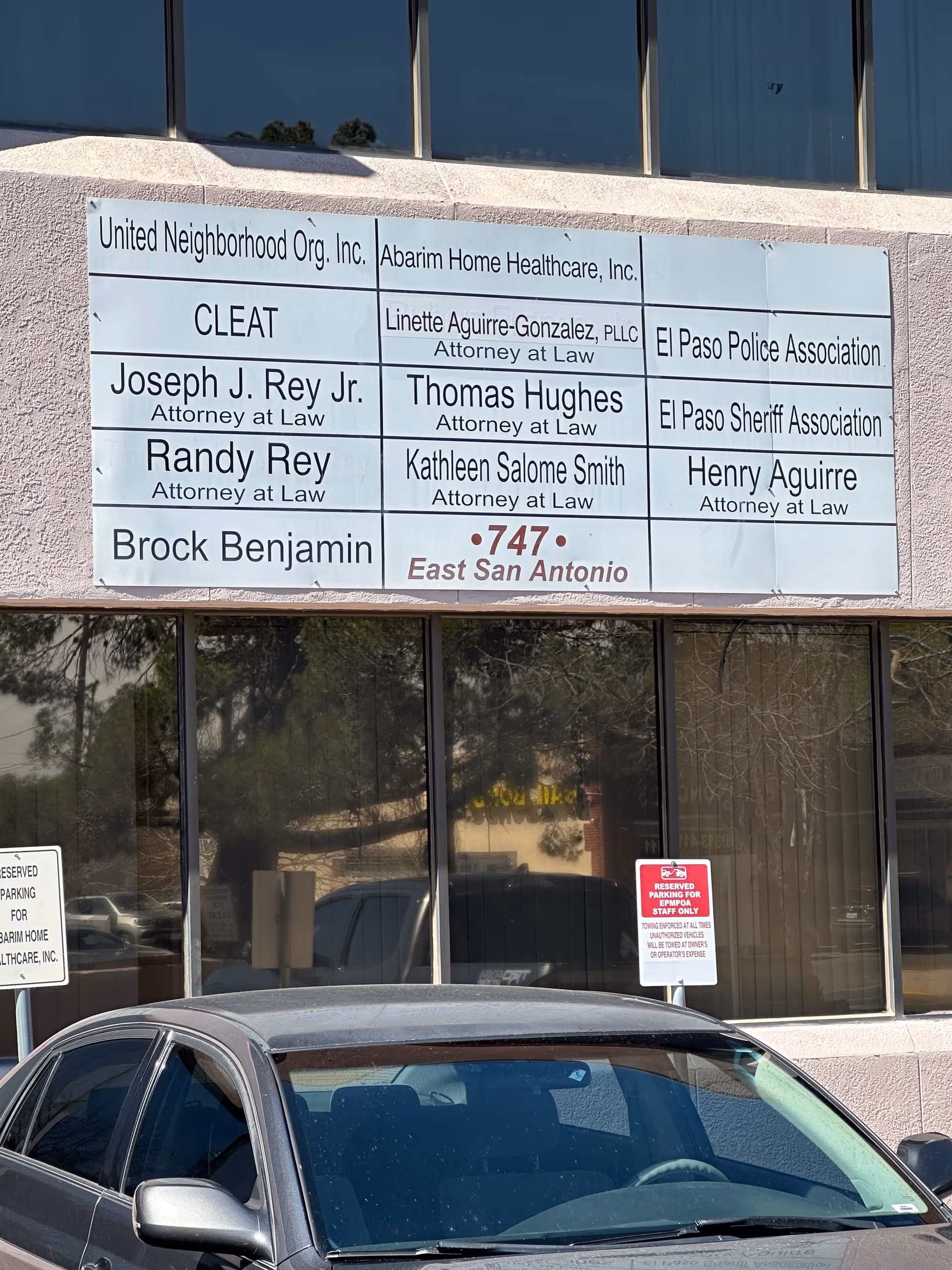 Facade of a building with a large sign listing multiple business names and a car.