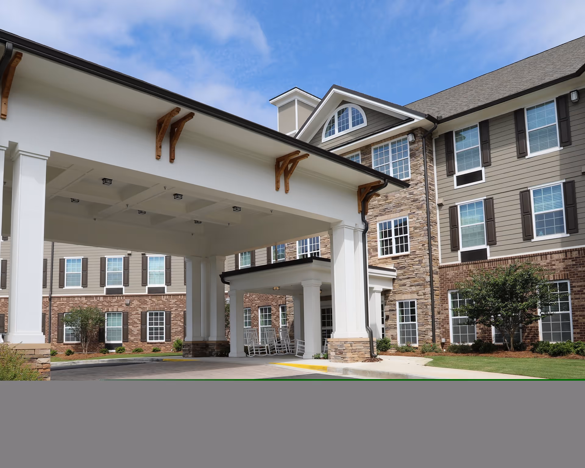 Exterior view of Canterfield of Kennesaw senior living facility showing a covered entrance with white pillars, rocking chairs, and a multi-story building with brick and stone facade under a partly cloudy sky.