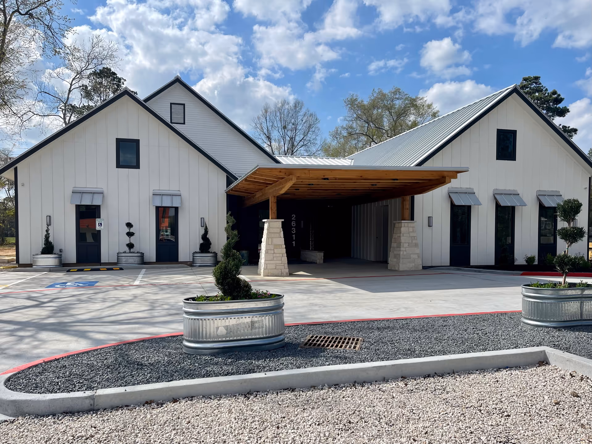 White, modern senior living building with a wooden entry canopy and paved driveway.
