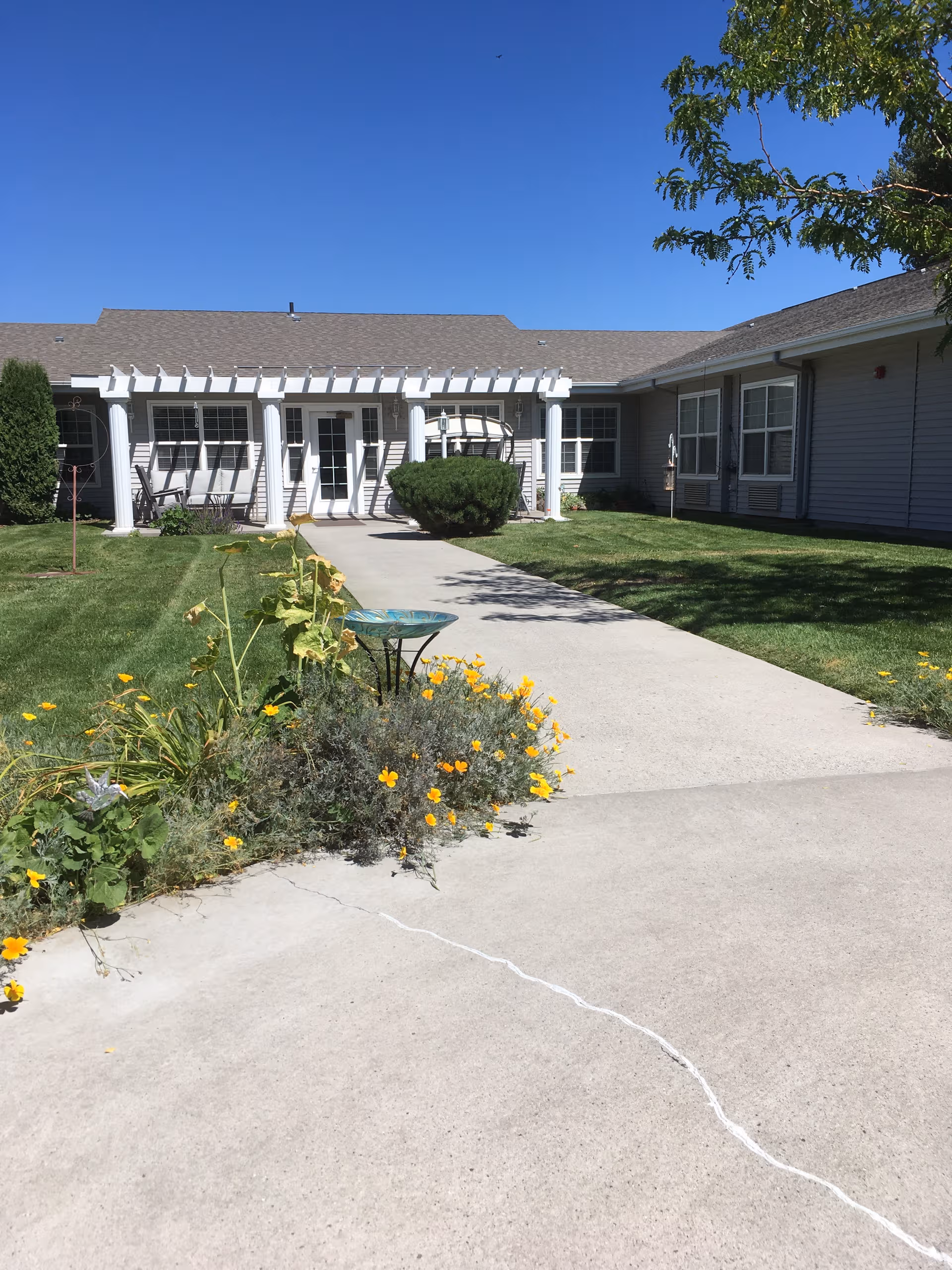 Front exterior of a senior living facility with a walkway and flowers.