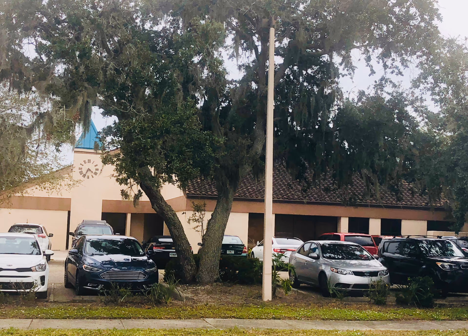 Exterior view of a senior care facility with a parking lot and large trees.