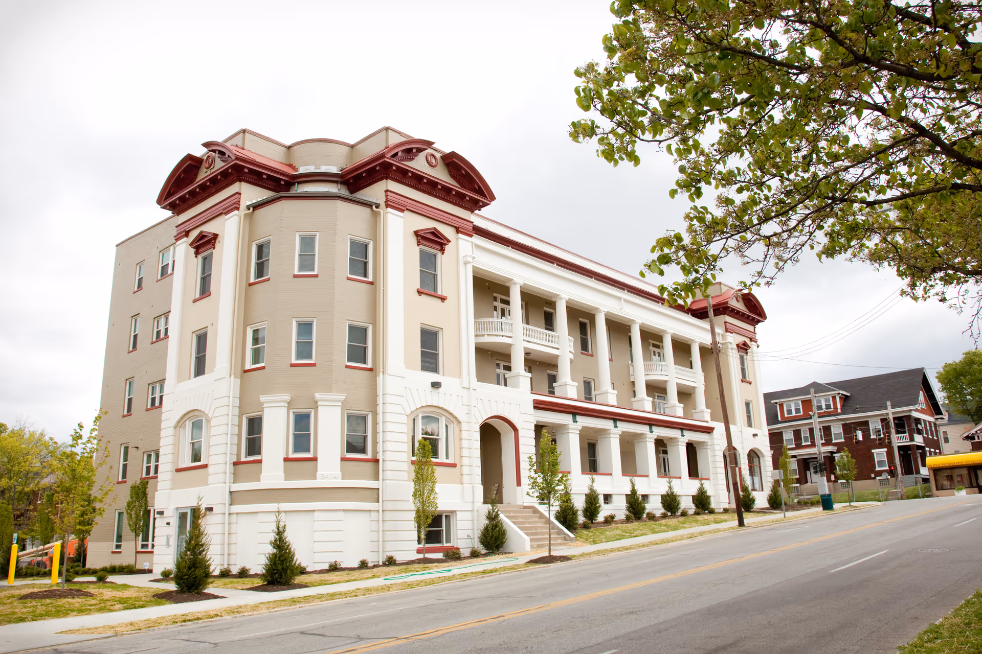 Large historic-style multi-story residential building with columns, balconies, and porches facing a tree-lined street.